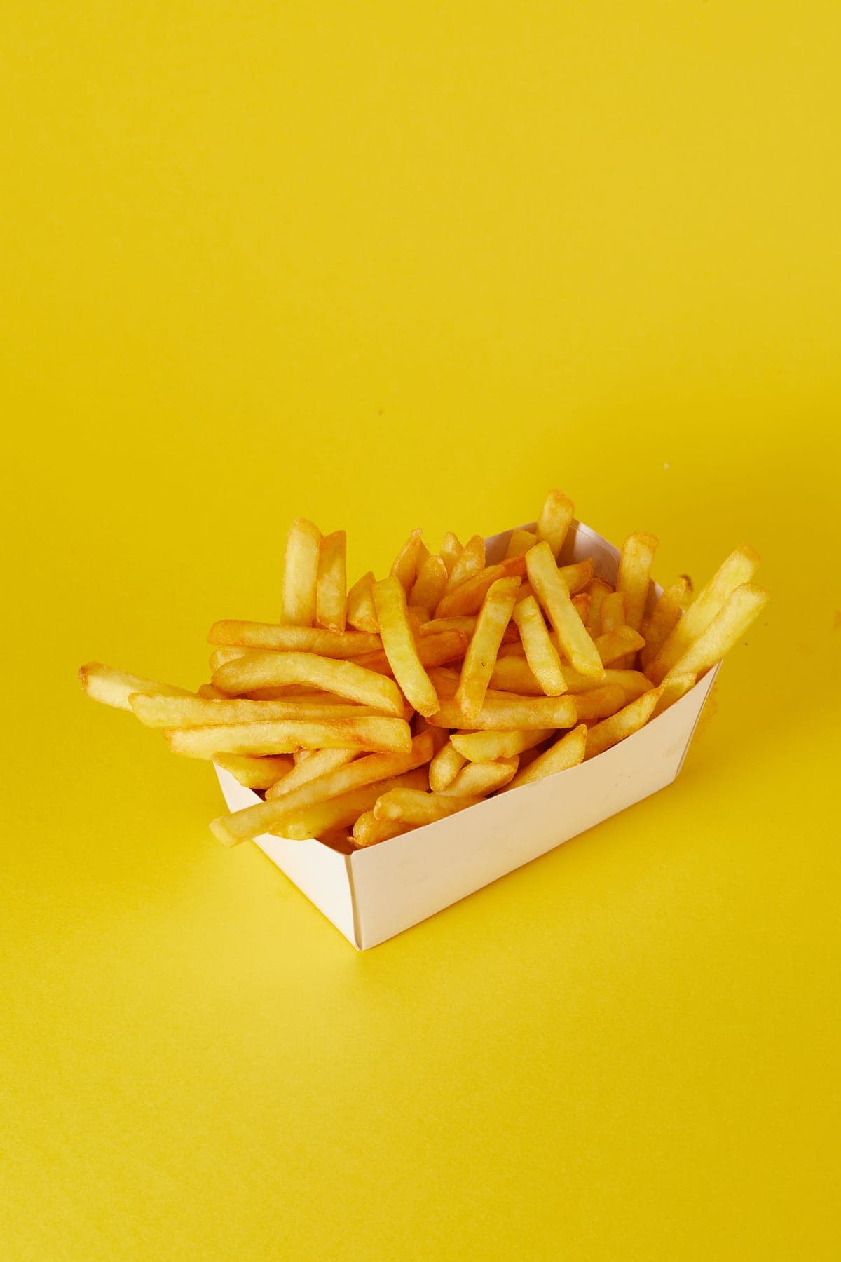 Een bakje frieten op een mosterdgele achtergrond
