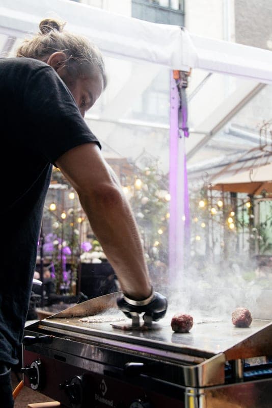 Een kok drukt een burger plat op een rokende bakplaat