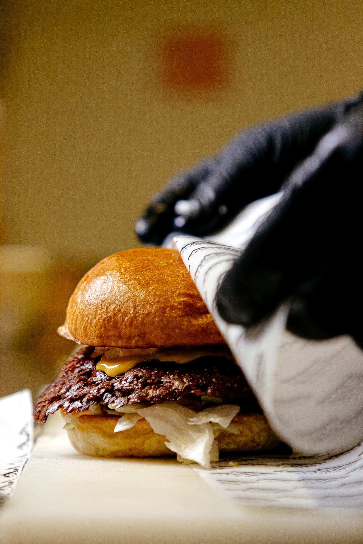 Een hand met handschoen houdt een smash burger in papier vast